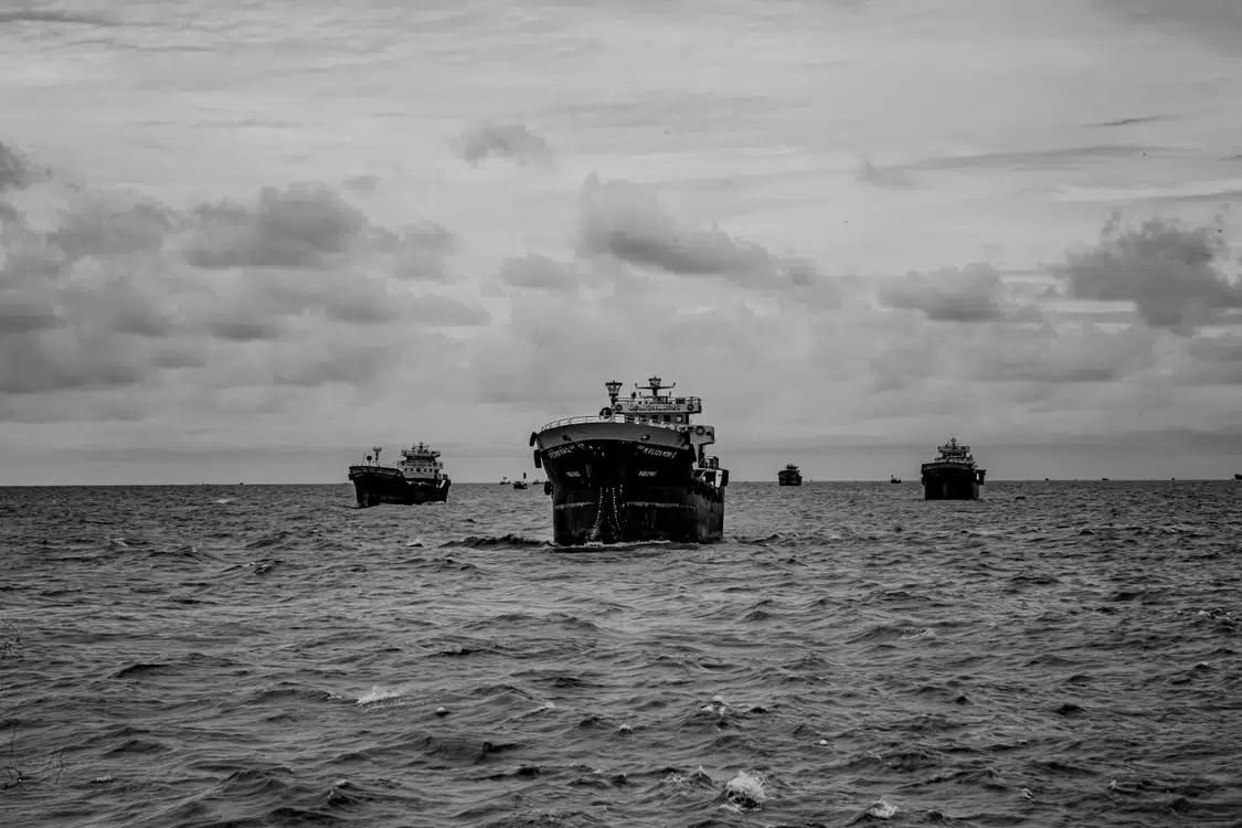 Large cargo ships navigating ocean waters under cloudy skies in black and white photography