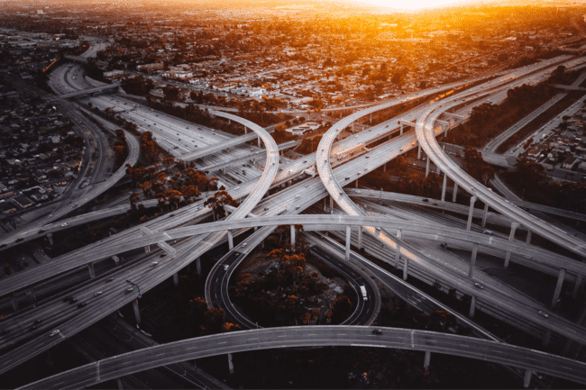 Expansive freeway interchange with multiple lanes at sunset, cityscape in the background