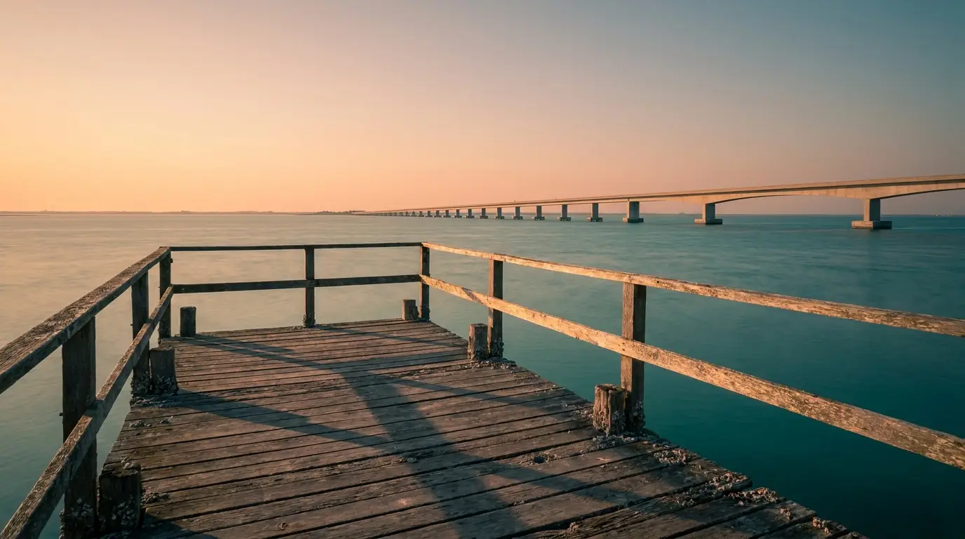 Wooden pier overlooking ocean with long bridge under warm sunset sky