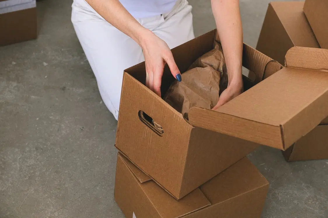 Person packing items into cardboard boxes on concrete floor