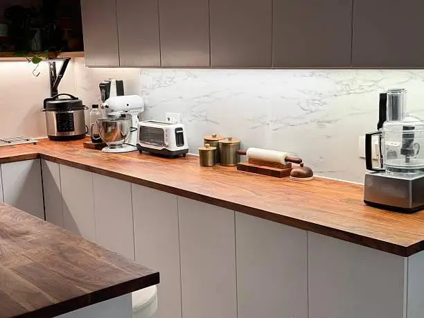 Kitchen countertop with mixer, toaster, and food processor, wooden surface under bright lighting