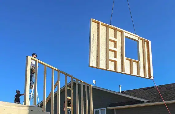 Construction workers installing prefabricated wall on building site under clear blue sky
